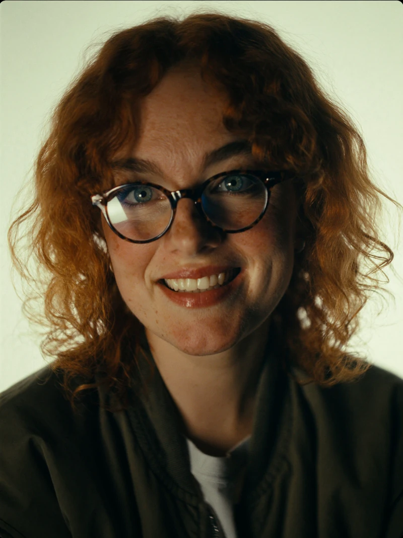AI-generated close-up of a fictional adult woman with freckles and a broad smile on a pale green backdrop, warm side light